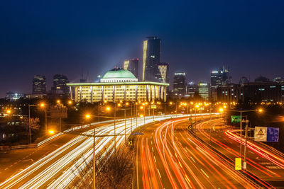 Light trails on road in city against sky at night