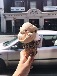 Cropped hand holding ice cream cone on street in city