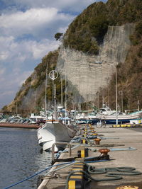 Boats moored on sea by mountain against sky