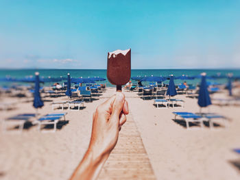 Midsection of person holding umbrella on beach against sky