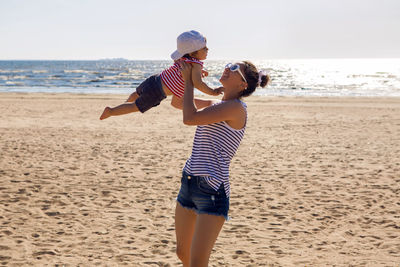 Mom in a striped t-shirt raises her son on the beach in the summer