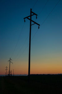 Low angle view of silhouette electricity pylon on field against clear sky
