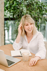 Smiling young woman using phone while sitting on table