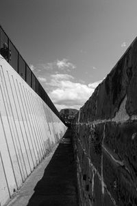 Empty footpath by wall against sky