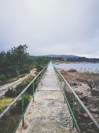 Footbridge amidst trees against sky