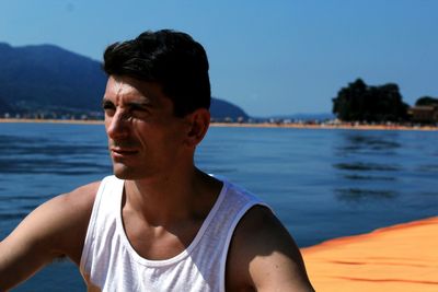 Mid adult man sitting on jetty over lake against blue sky