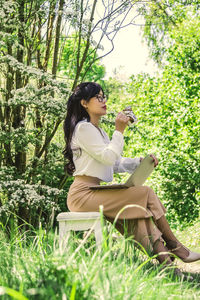 Woman holding laptop while sitting by plants