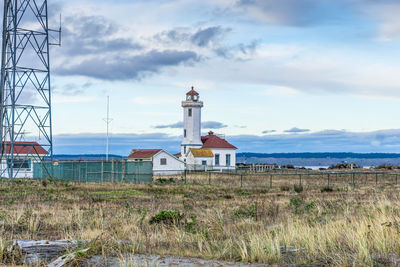 Lighthouse on field by building against sky