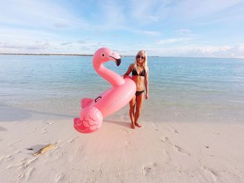 Full length of woman holding inflatable ring while standing on shore at beach