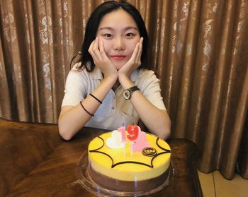 Portrait of smiling girl with cake sitting at home