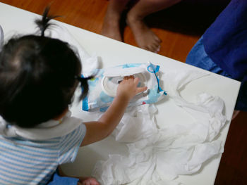 Rear view of girl pulling tissue paper while sitting on table