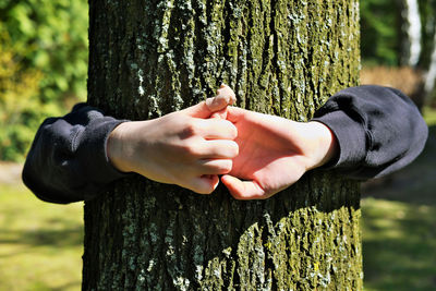 Midsection of man holding hands against tree trunk