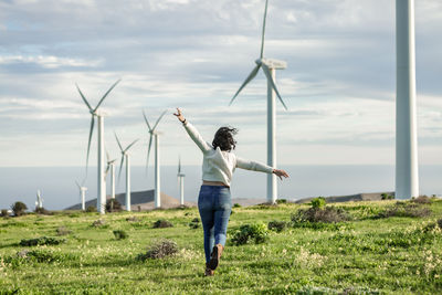 Rear view of woman running against wind turbines
