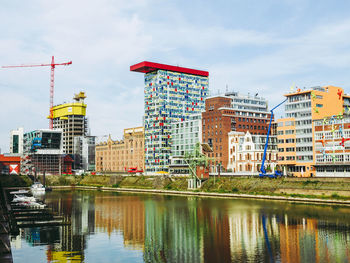 Buildings by river against sky in city