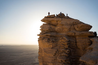 From below group of anonymous travelers contemplating colorful sundown while visiting the edge of the world in saudi arabia