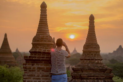 Rear view of man photographing while standing by stupas during sunset