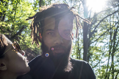 Portrait of bearded man with woman against trees on sunny day