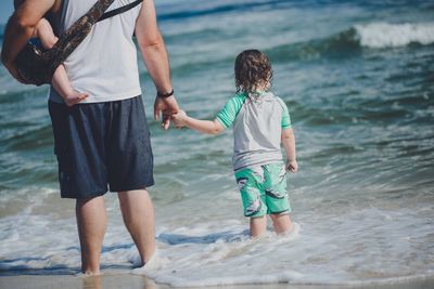 Rear view of father with children standing on shore at beach