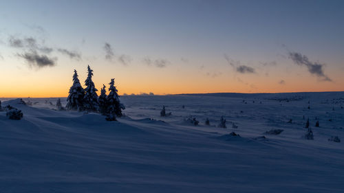 Snow covered landscape against sky during sunset