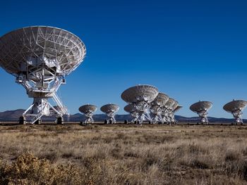 Low angle view of satellite dishes on field against clear blue sky