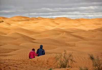Rear view of men on sand dune in desert against sky
