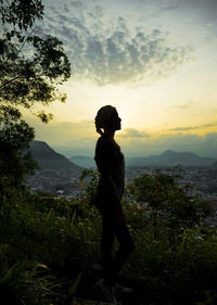 Silhouette teenage girl standing on mountain against sky during sunset