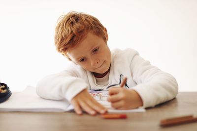 Close-up of boy writing on book against white background