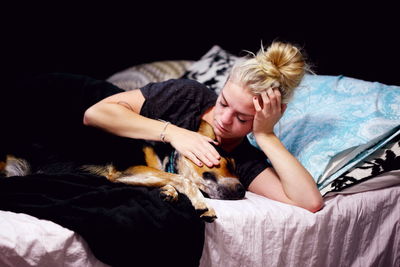 Woman petting pembroke welsh corgi while lying on bed in bedroom