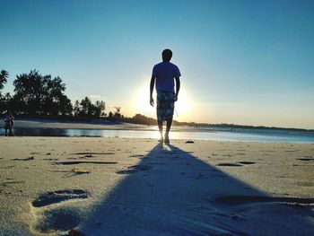 Rear view of man on beach against clear sky