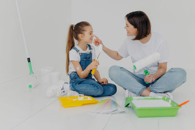 Playful woman applying paint on daughter nose against white wall