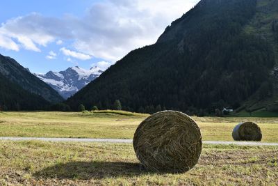 Hay bales on field by mountains against sky
