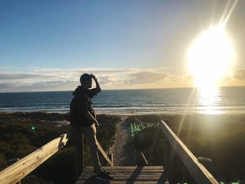 Man standing on railing against sea during sunset