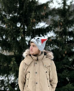 Young woman looking away while standing against trees during winter