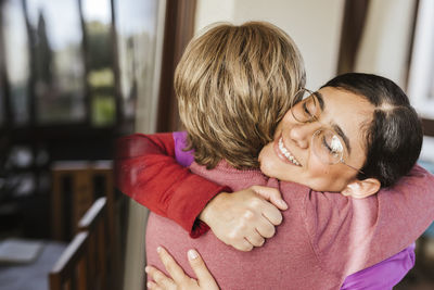 Happy caregiver hugging senior woman at home