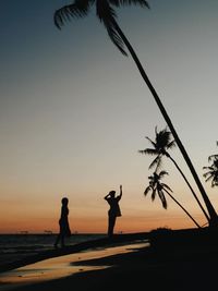 Silhouette people on beach against sky during sunset