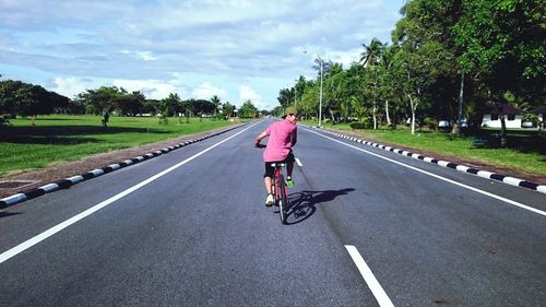 Man riding bicycle on road against sky