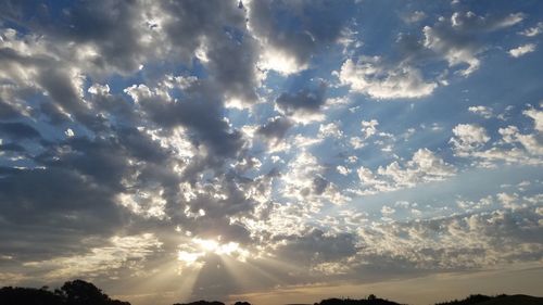 Low angle view of sunlight streaming through clouds