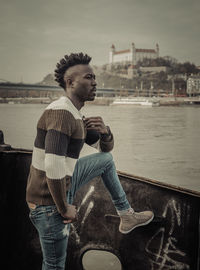 Young man standing by river against sky