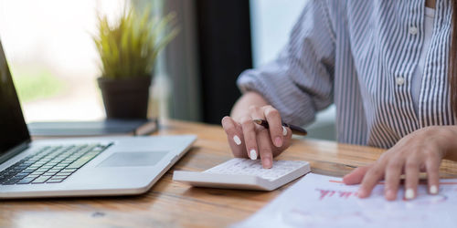 Close up business woman using calculator and laptop for do math finance on wooden desk in office