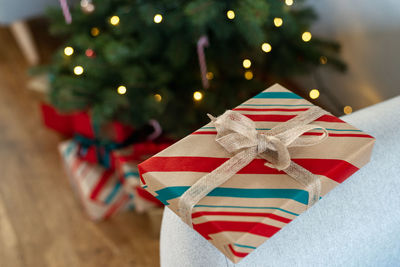 A beautifully wrapped gift, decorated with a ribbon, lies on the background of a christmas tree.