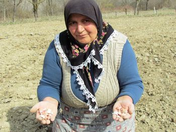 Portrait of woman holding garlic bulbs while kneeling on ground