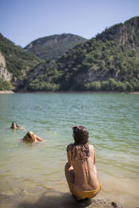 Rear view of shirtless woman in lake against mountain