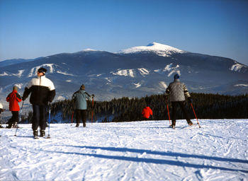 Rear view of men skiing on snowcapped mountain against sky