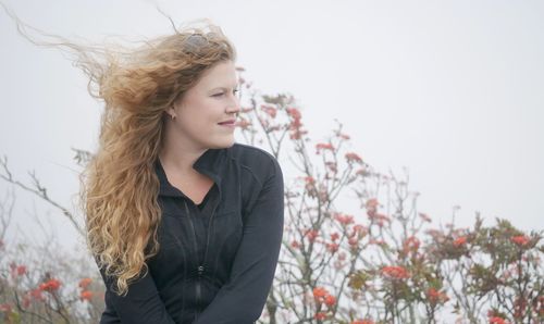 Young woman looking away while standing against sky