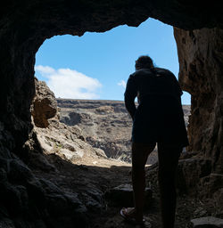 Rear view of man standing on rock against sky