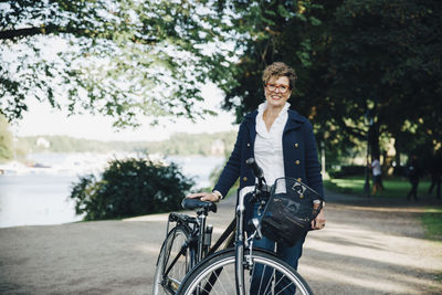 Portrait of smiling senior woman with bicycle standing in park