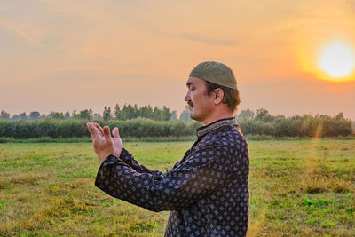 Side view of man standing on field against sky during sunset