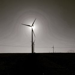 Low angle view of wind turbines on field against sky