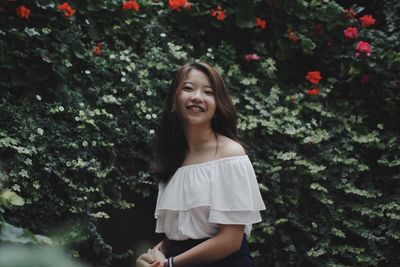 Portrait of smiling young woman standing against plants at park