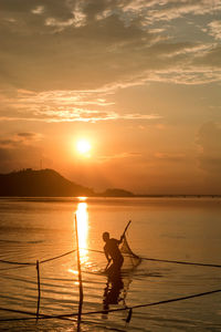 Silhouette person fishing on river against sky during sunset